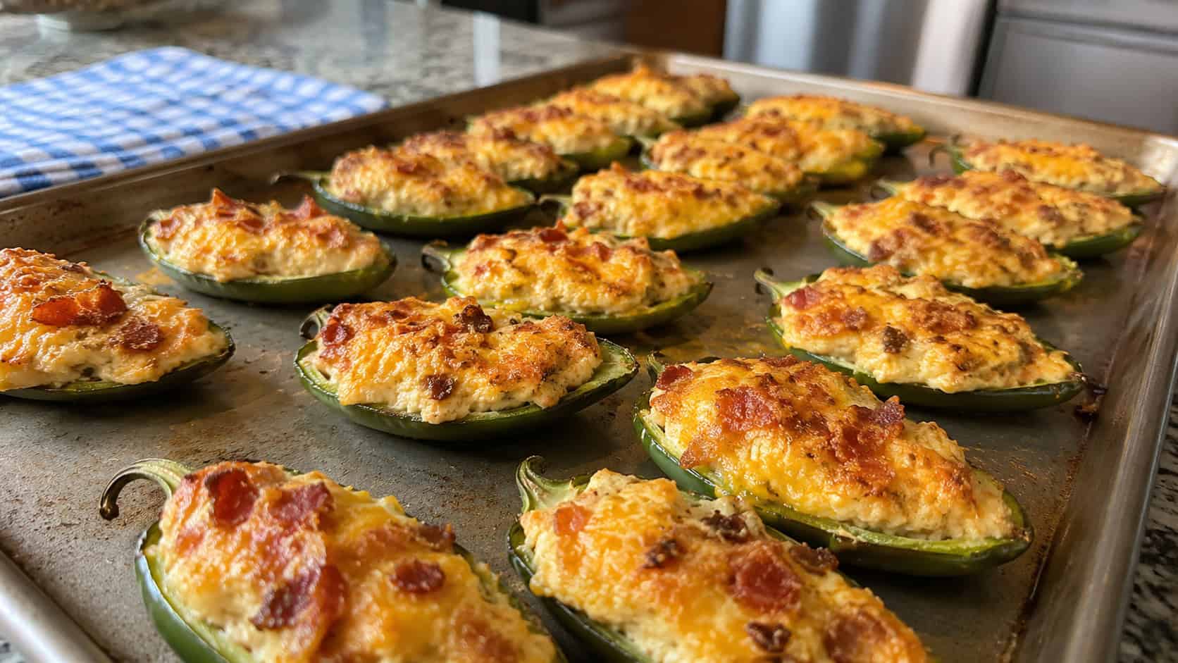 stuffed jalapeño halves with golden cheesy bacon filling lined up on a wide baking sheet, set on a kitchen counter, natural light, shallow depth of field, landscape orientation