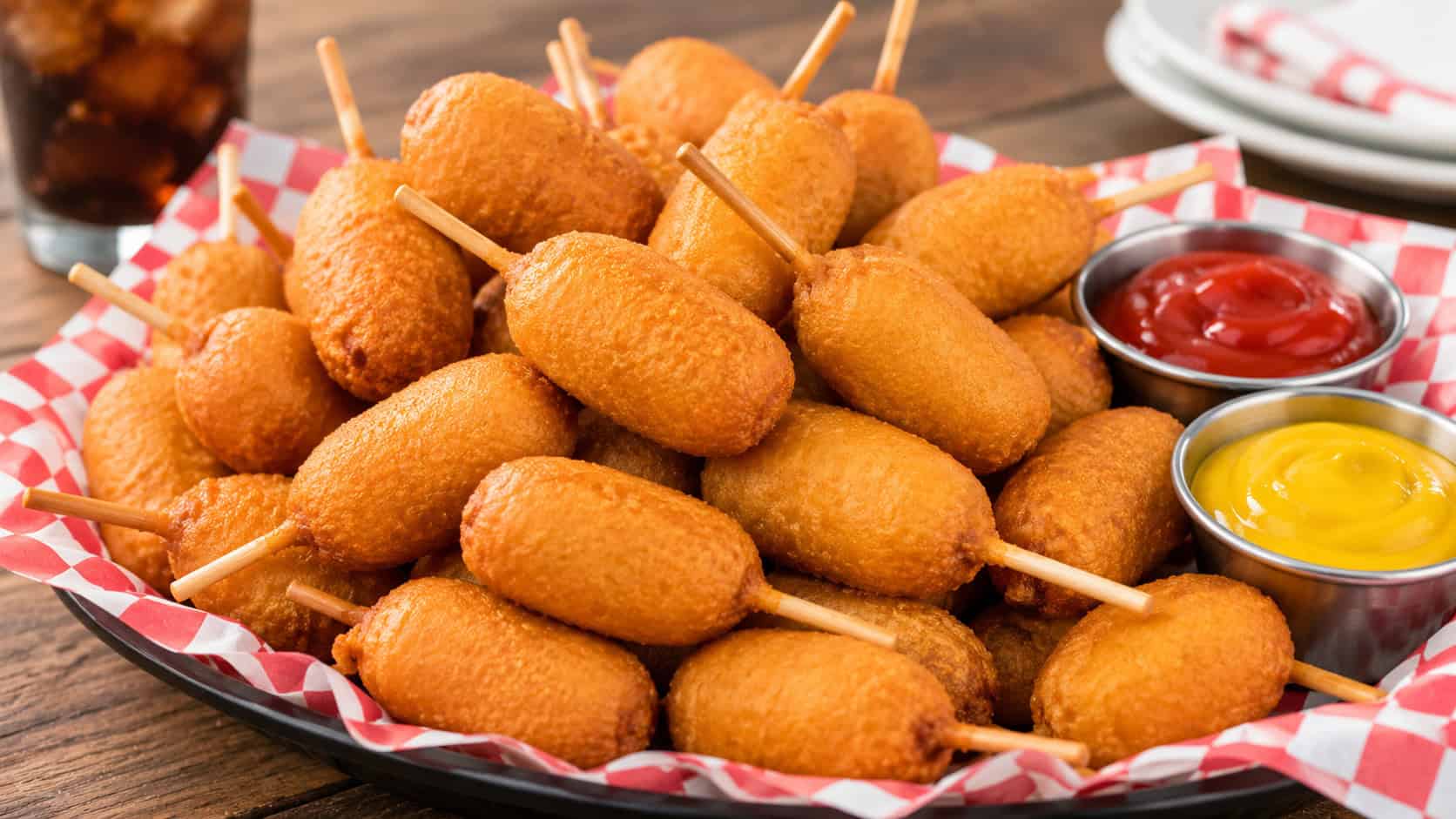a wide pile of golden mini corn dogs on toothpicks with ketchup and mustard for dipping, in a wide horizontal shot, on a casual diner-style platter, natural light, shallow depth of field, landscape orientation