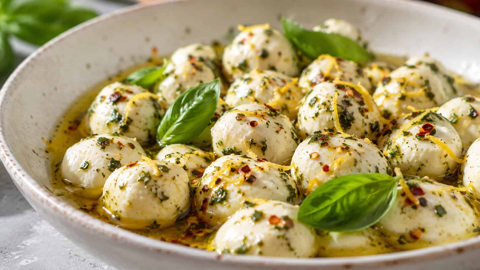 marinated mozzarella balls in herb-flecked olive oil in a shallow bowl, wide horizontal shot, fresh basil and chili flakes, lemon zest, bright natural light, shallow depth of field, landscape orientation
