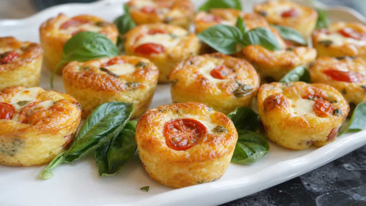 mini crustless caprese quiches with tomato and mozzarella arranged on a platter, wide horizontal shot, golden puffed tops, fresh basil garnish, bright natural light, shallow depth of field, landscape orientation