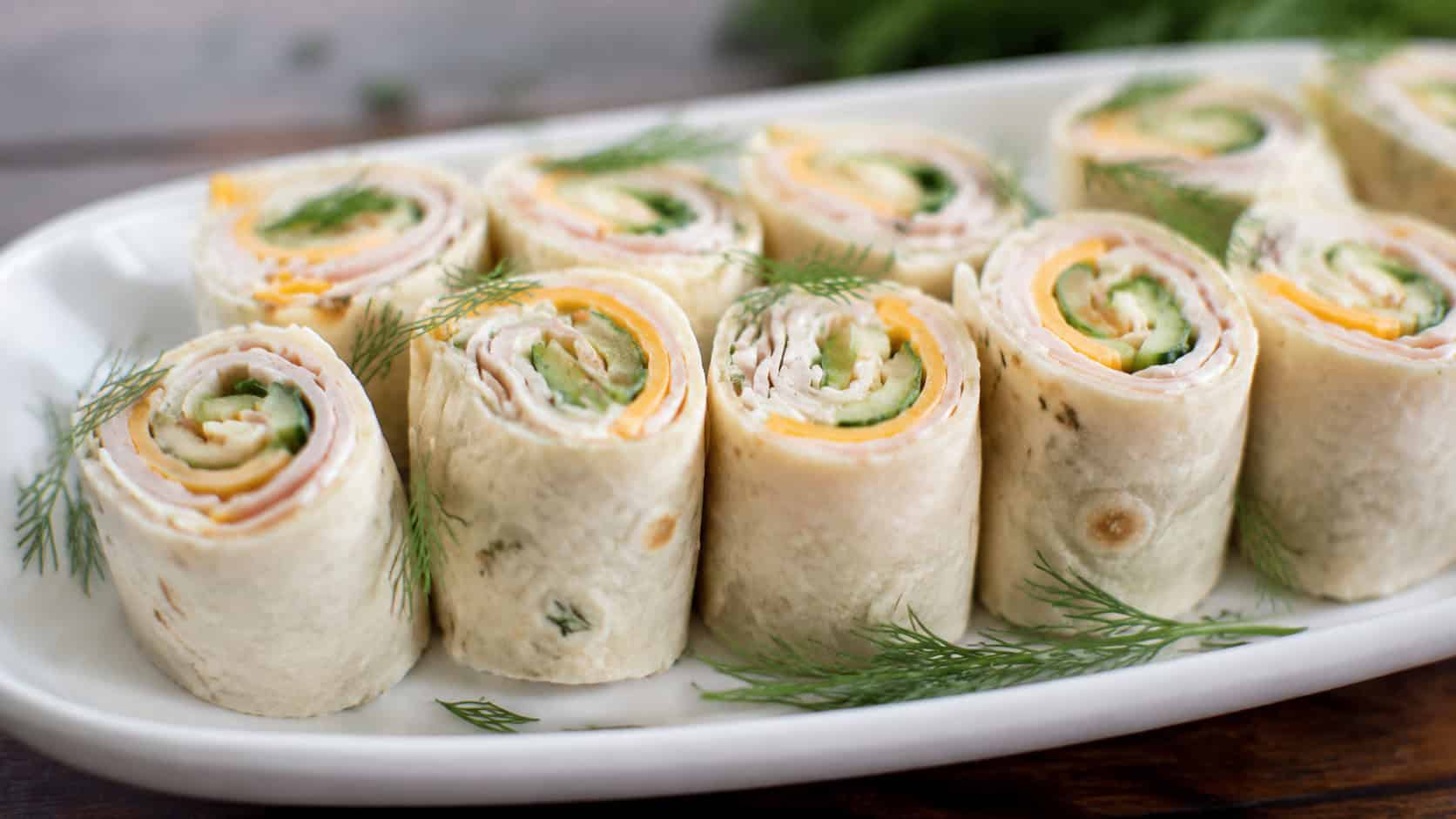 turkey and cheese roll-ups sliced and standing upright on a white plate in a wide horizontal shot, cucumber peeking through, fresh dill garnish, bright natural light, shallow depth of field, landscape orientation