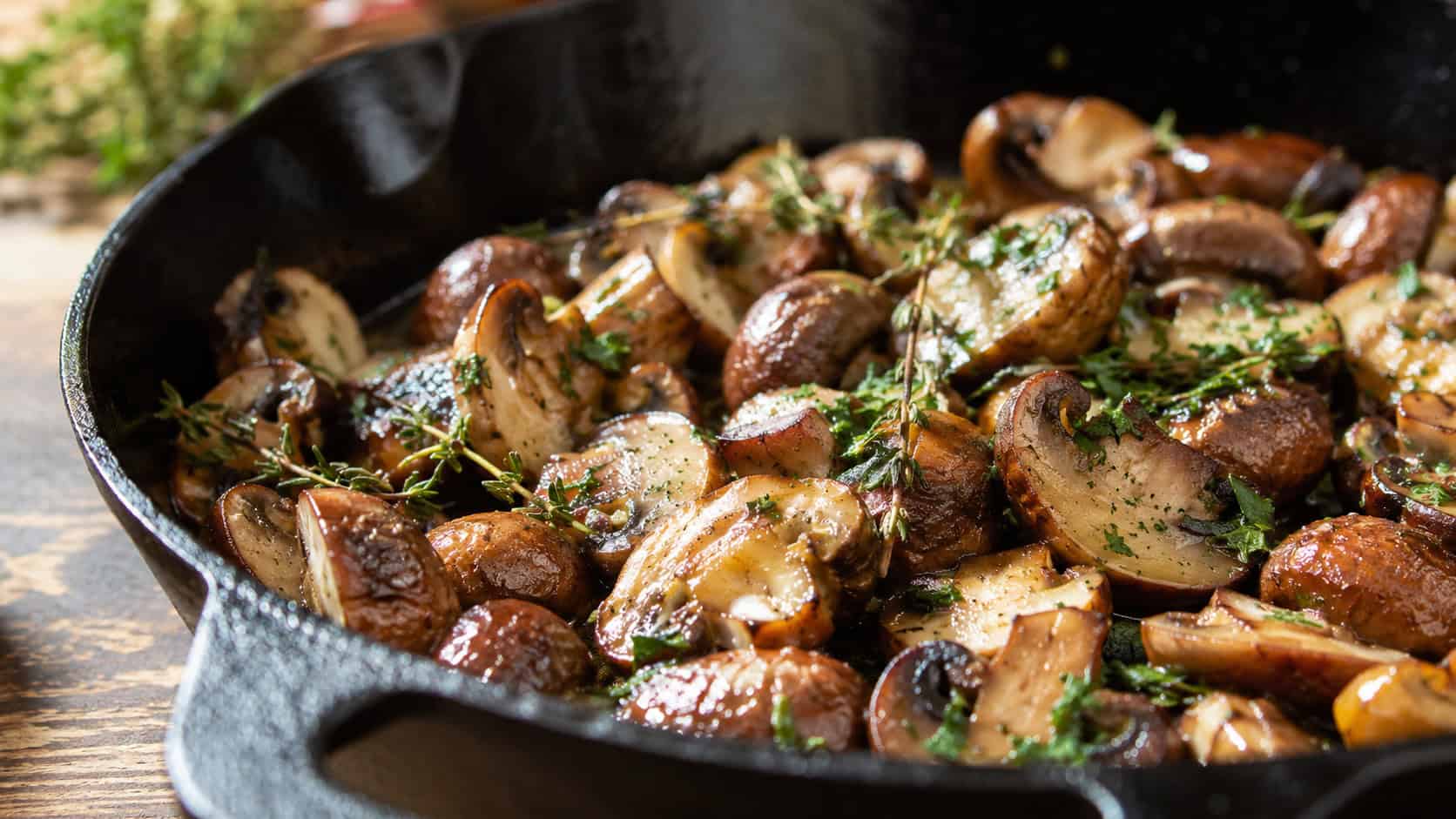 glistening garlic butter mushrooms in a cast iron skillet in a wide horizontal shot, golden edges, fresh thyme and parsley scattered, warm natural light, shallow depth of field, landscape orientation