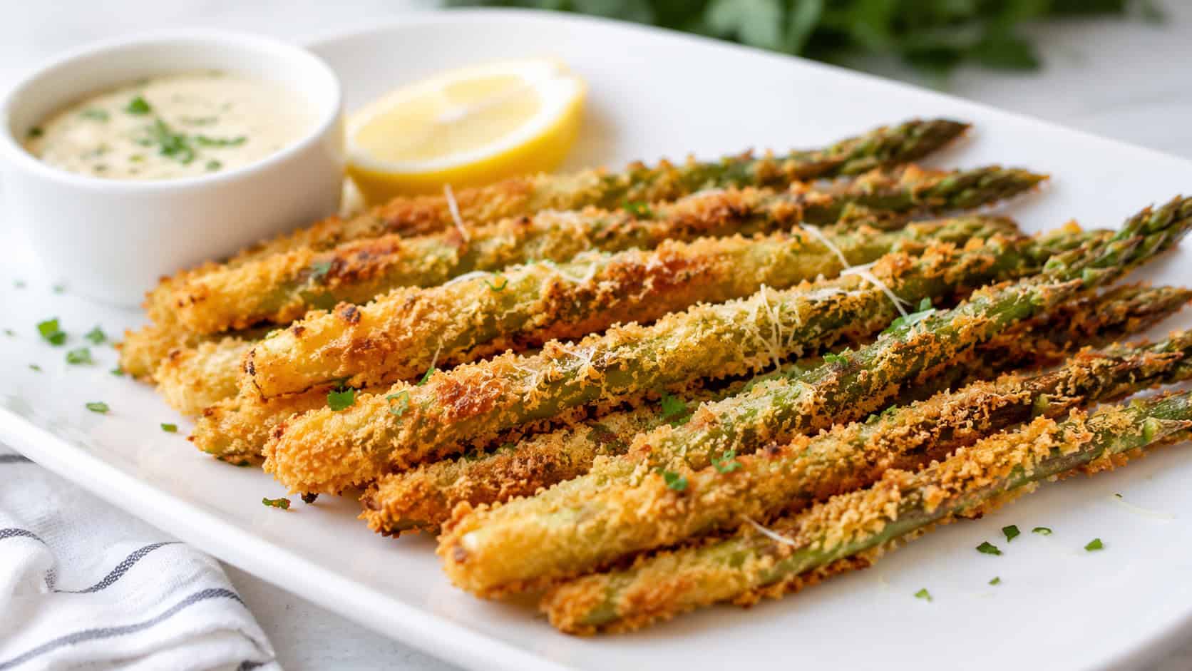 crispy parmesan asparagus fries fanned out on a white plate in a wide horizontal shot, golden coating, small bowl of dip, lemon wedge, bright natural light, shallow depth of field, landscape orientation