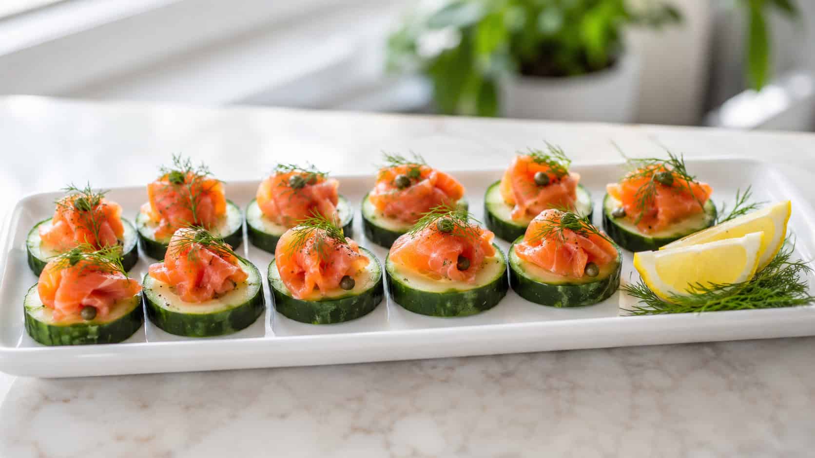 salmon cucumber bites arranged in neat rows on a white platter in a wide horizontal shot, fresh dill sprigs, lemon wedge to the side, bright airy natural light, shallow depth of field, landscape orientation