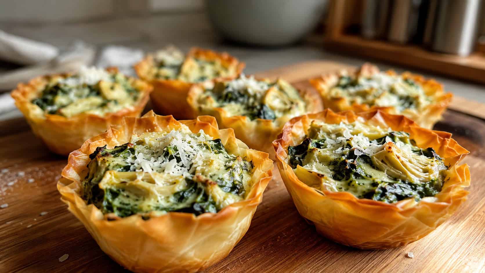 spinach and artichoke phyllo tartlets on a wooden board, golden crisp pastry cups filled with bubbling creamy green spinach-artichoke filling flecked with melted cheese, a few flakes of parmesan on top, warm natural light, shallow depth of field, cozy kitchen counter