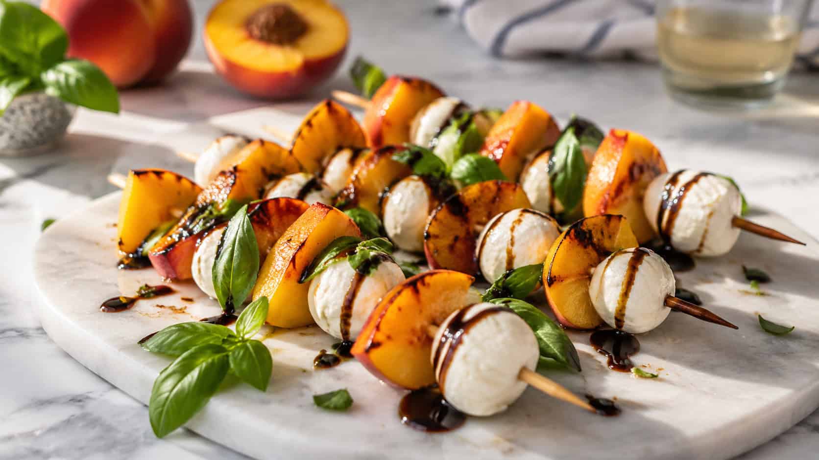 peach and mozzarella skewers on a marble board in a wide horizontal shot, golden peach wedges and white mozzarella, dark balsamic glaze drizzled across, fresh basil, soft summer light, shallow depth of field, landscape orientation