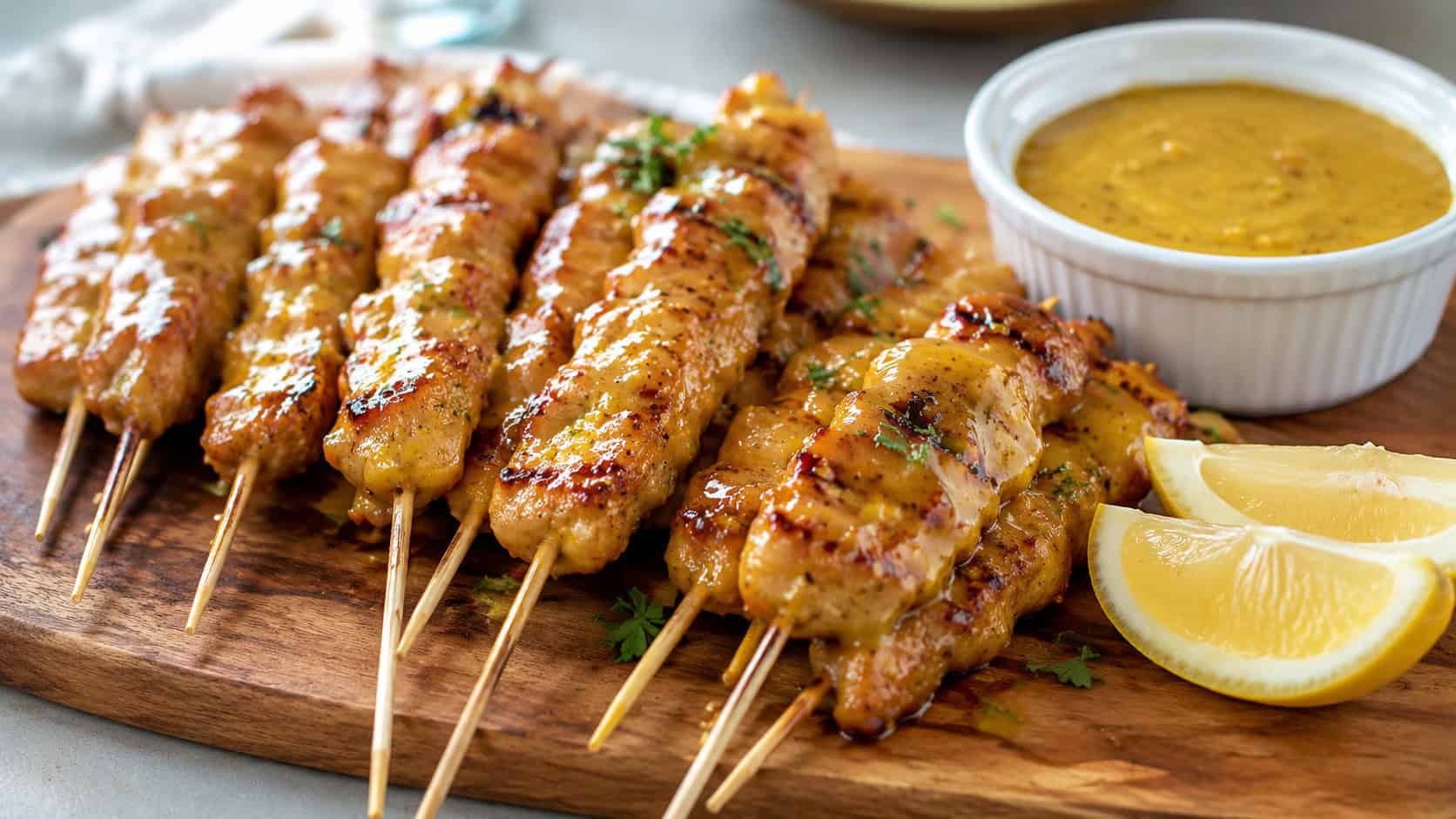 golden honey mustard chicken skewers fanned across a wooden serving board in a wide horizontal shot, glossy amber glaze, ramekin of extra sauce and lemon wedges beside them, bright natural light, shallow depth of field, landscape orientation