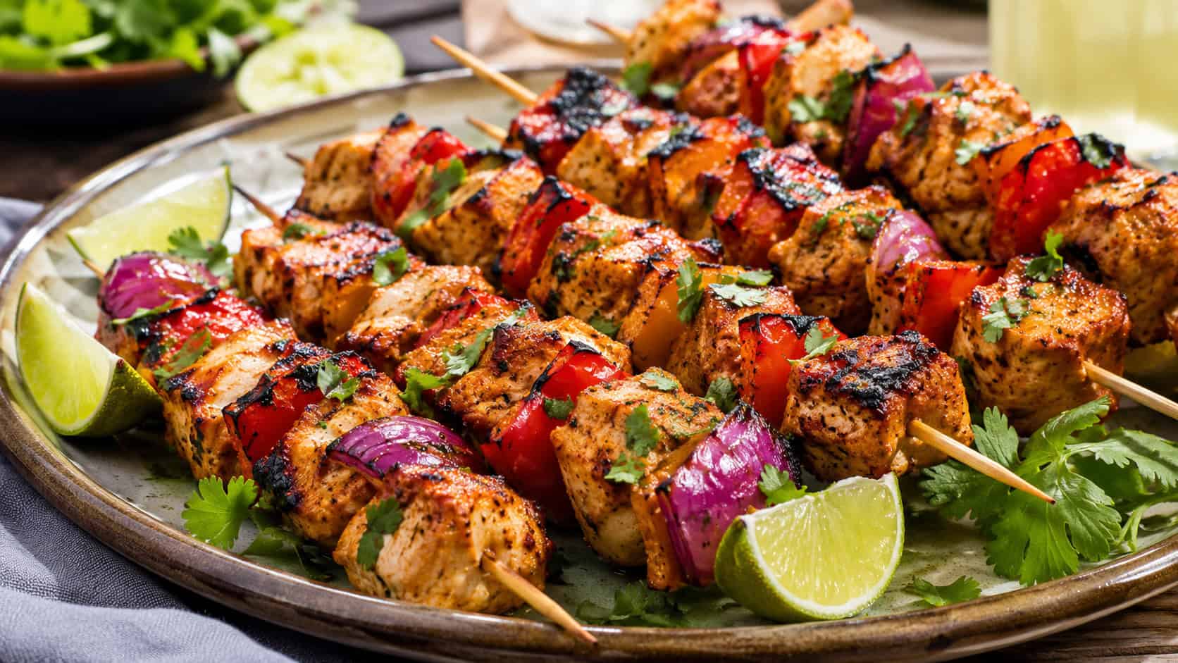 colorful chili lime chicken and vegetable skewers on a ceramic platter in a wide horizontal shot, charred red peppers and onion, lime wedges and cilantro scattered around, bright natural light, shallow depth of field, landscape orientation