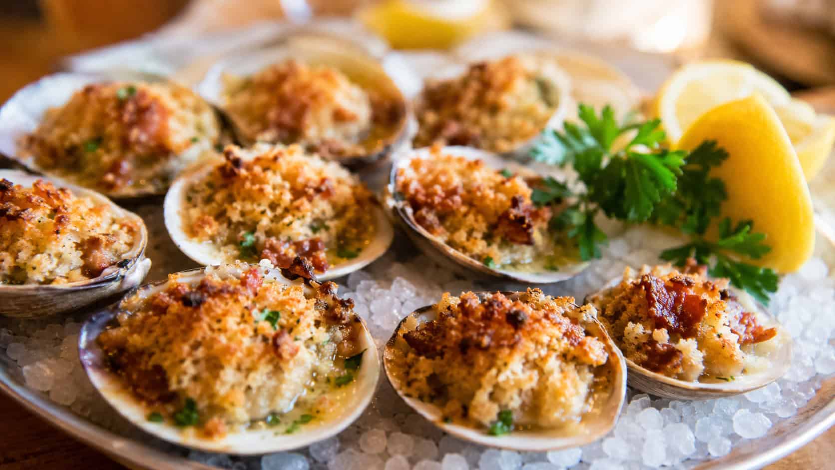 clams casino topped with golden bacon breadcrumbs on the half shell in a wide horizontal shot, on rock salt on a platter with lemon and parsley, warm savory light, shallow depth of field, landscape orientation