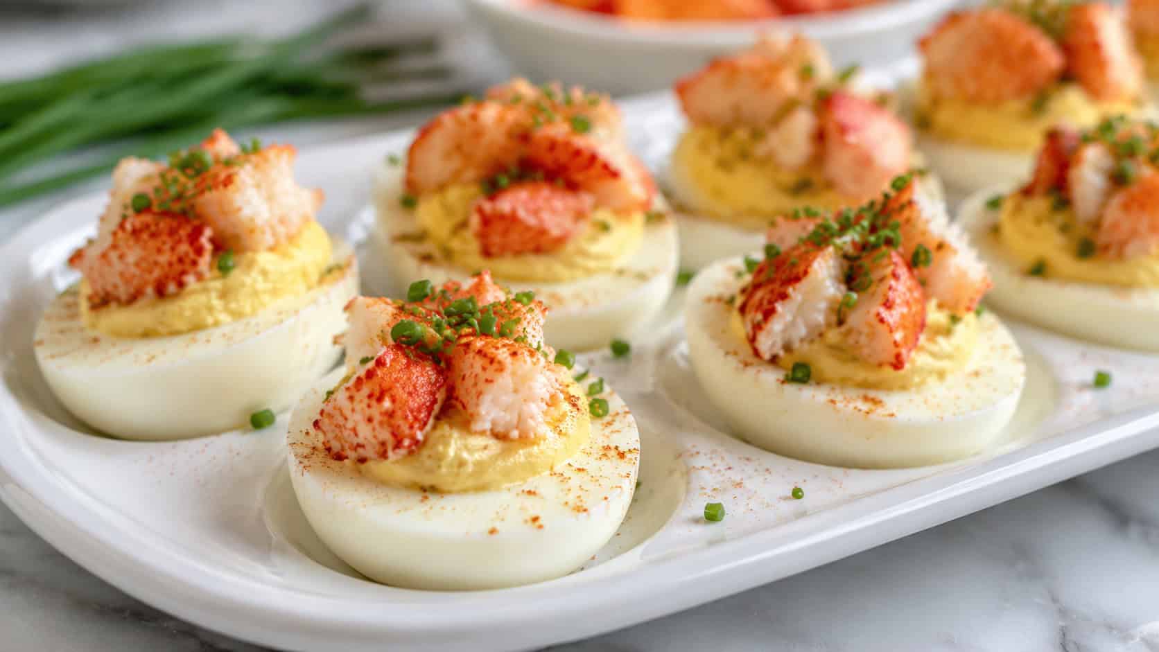deviled eggs topped with chunks of lobster and chives in a wide horizontal shot, arranged on a white deviled egg platter with paprika dusting, bright fresh light, shallow depth of field, landscape orientation