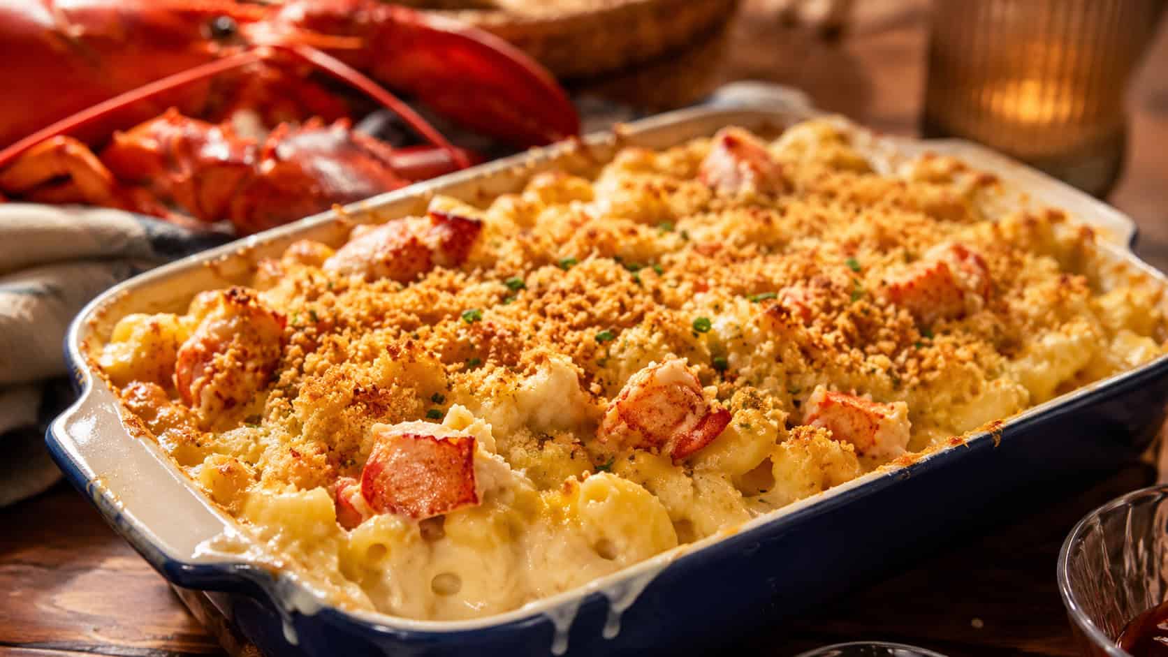 bubbling lobster mac and cheese with a golden panko crust in a baking dish in a wide horizontal shot, with chunks of lobster visible on a wooden table, warm cozy light, shallow depth of field, landscape orientation