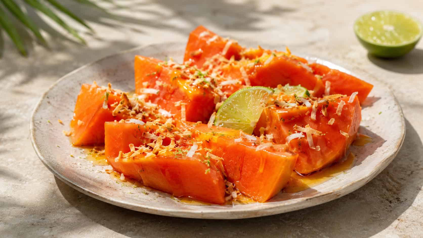 bright orange papaya wedges drizzled with honey and lime in a wide horizontal shot, topped with toasted coconut on a pale stone plate, sunny natural light, shallow depth of field, landscape orientation