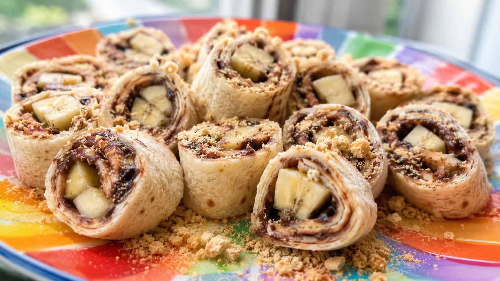 chocolate hazelnut and banana pinwheels in a wide horizontal shot, fanned out on a colorful plate with crushed graham crackers, bright natural light, shallow depth of field, landscape orientation