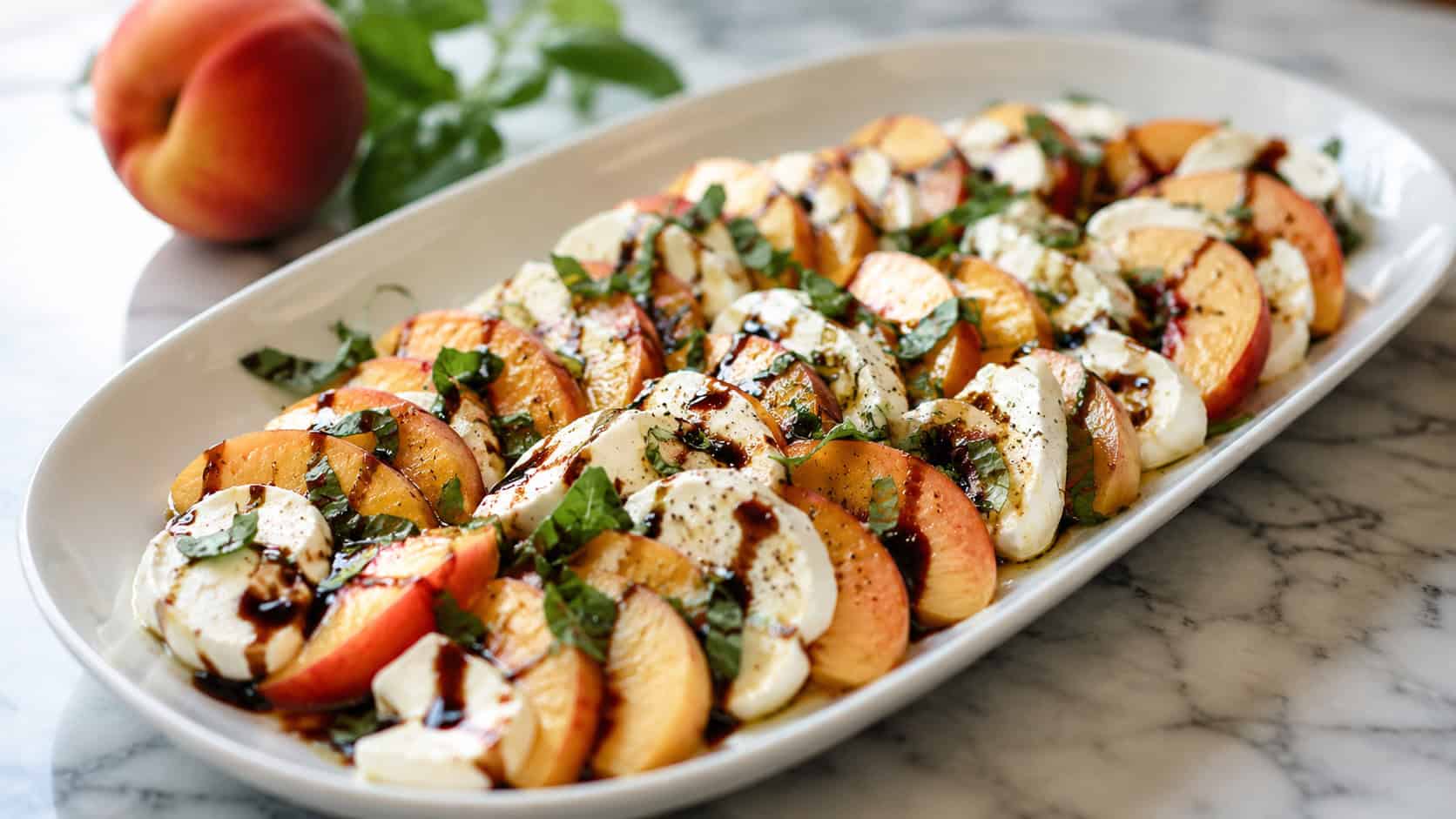 a wide oval platter of sliced peach and mozzarella caprese salad in a horizontal shot, scattered with basil and balsamic drizzle on a marble counter, bright natural light, shallow depth of field, landscape orientation