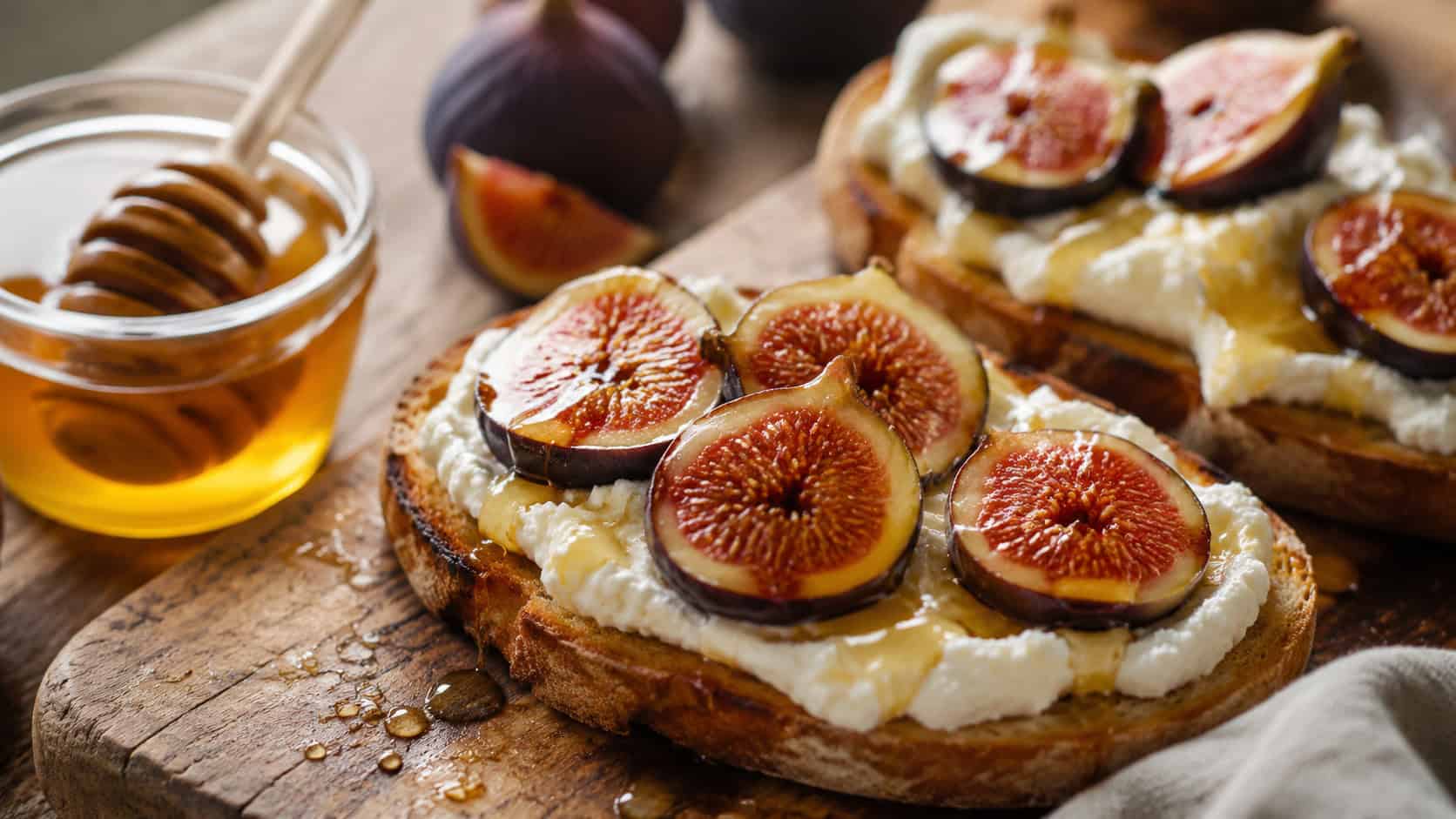 ricotta toast topped with fresh fig halves and honey in a wide horizontal shot, on a rustic wooden board with a honey jar, warm natural light, shallow depth of field, landscape orientation