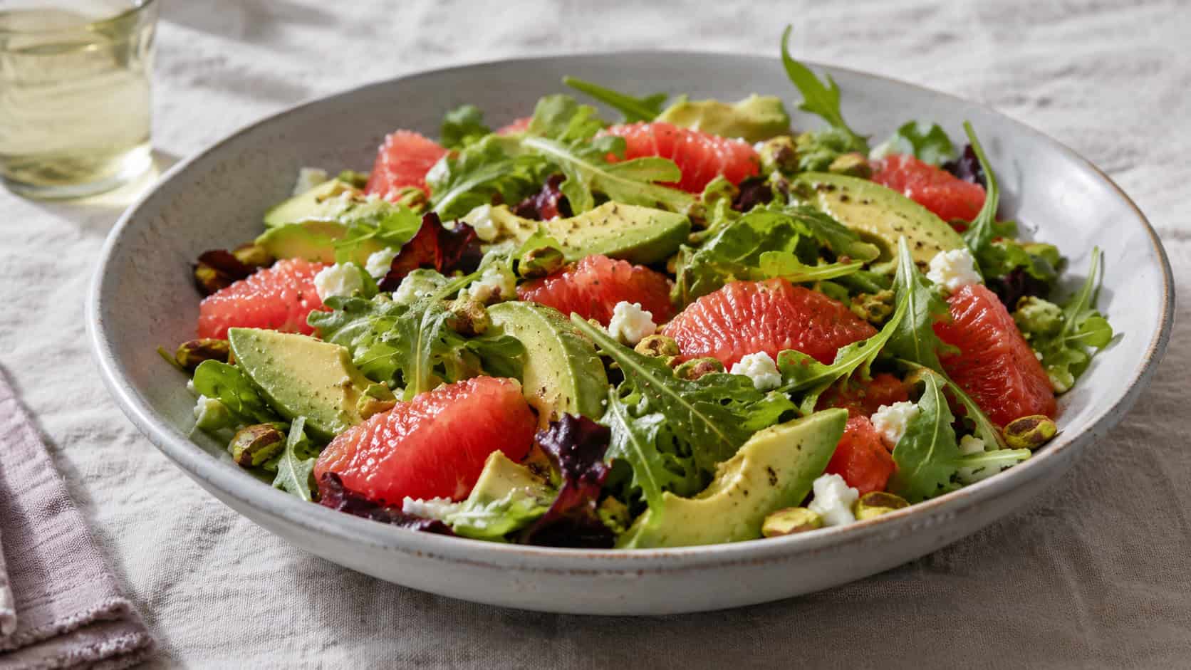 an avocado and grapefruit salad over greens in a wide horizontal shot, served on a large shallow bowl on a linen tablecloth, soft natural light, shallow depth of field, landscape orientation