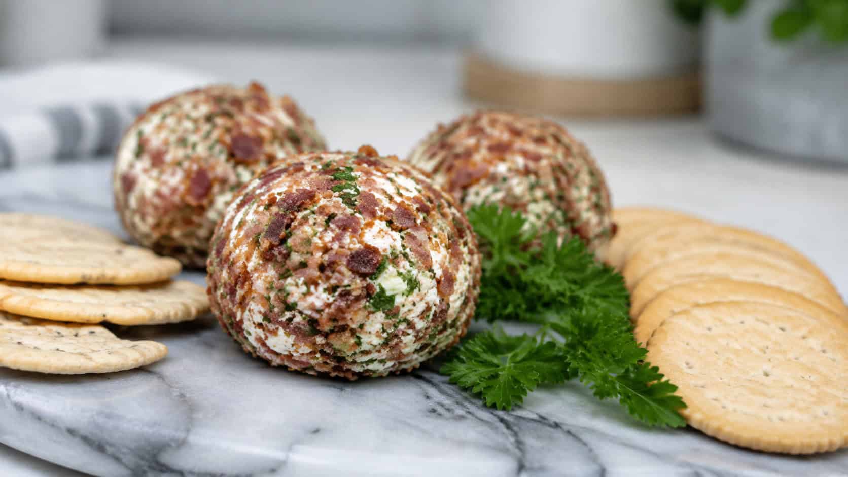 bacon and herb goat cheese balls on a wide marble board shot horizontally, creamy spheres coated in crumbled bacon and green herbs, crackers fanned around them and a sprig of parsley, soft natural light, shallow depth of field, landscape orientation