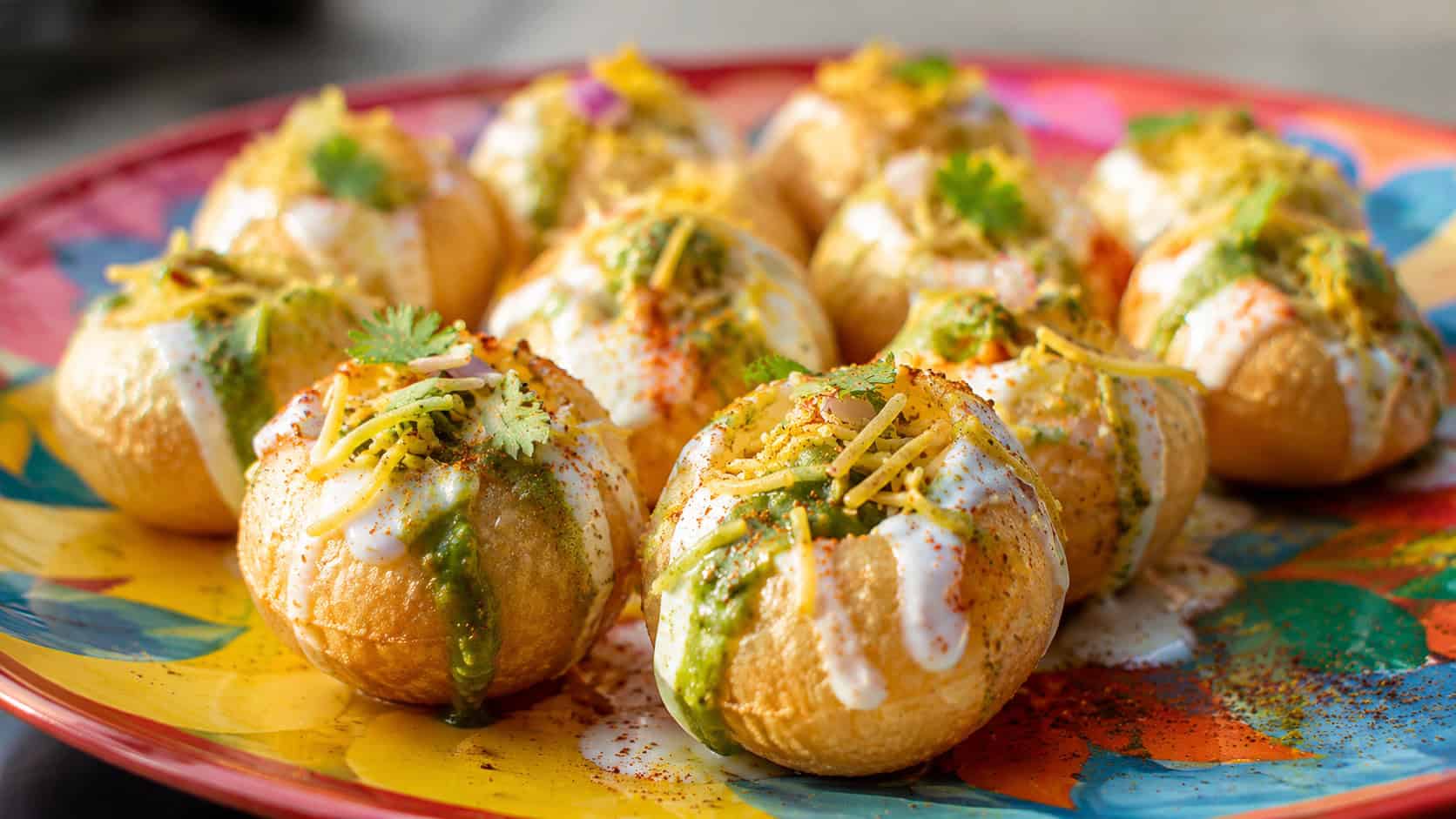 dahi puri shells filled with creamy yogurt, chutney, and crunchy sev in a wide horizontal shot, arranged on a colorful plate sprinkled with spice, bright natural light, shallow depth of field, landscape orientation