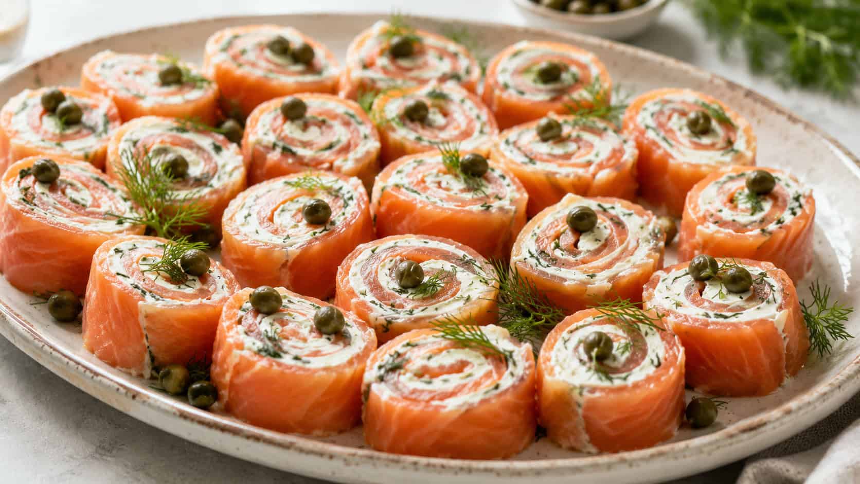 a wide platter of smoked salmon pinwheels showing spirals of pink salmon and white cream cheese, garnished with dill and capers, on a light ceramic plate, bright natural light, shallow depth of field, landscape orientation