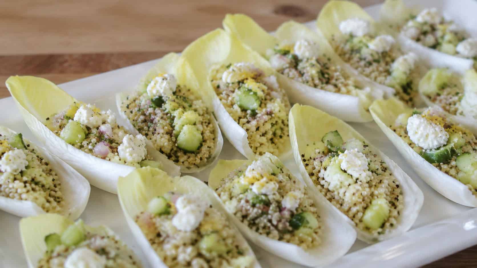 endive leaves filled with lemony quinoa salad, cucumber, and feta arranged on a platter, in a wide horizontal shot, natural light, shallow depth of field, landscape orientation