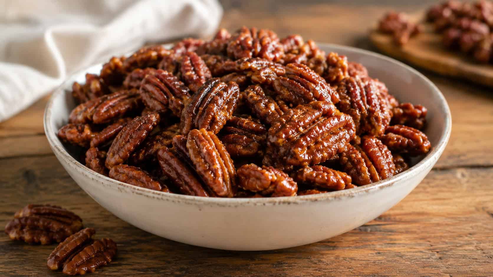 a bowl of glazed sweet and spicy pecans with a glossy cinnamon coating on a rustic table, in a wide horizontal shot, natural light, shallow depth of field, landscape orientation