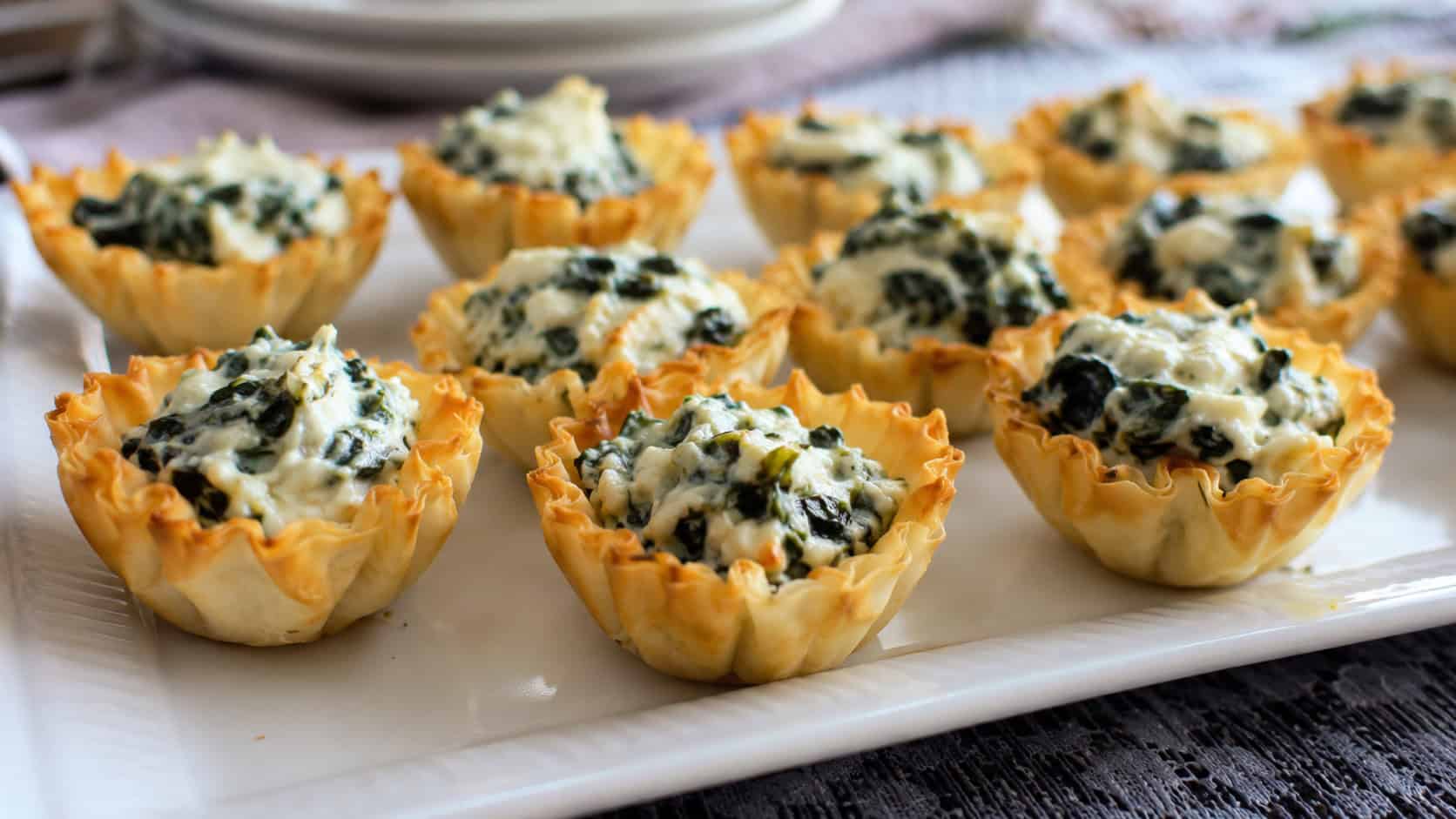 golden phyllo cups filled with creamy ricotta and spinach arranged on a serving platter, in a wide horizontal shot, natural light, shallow depth of field, landscape orientation