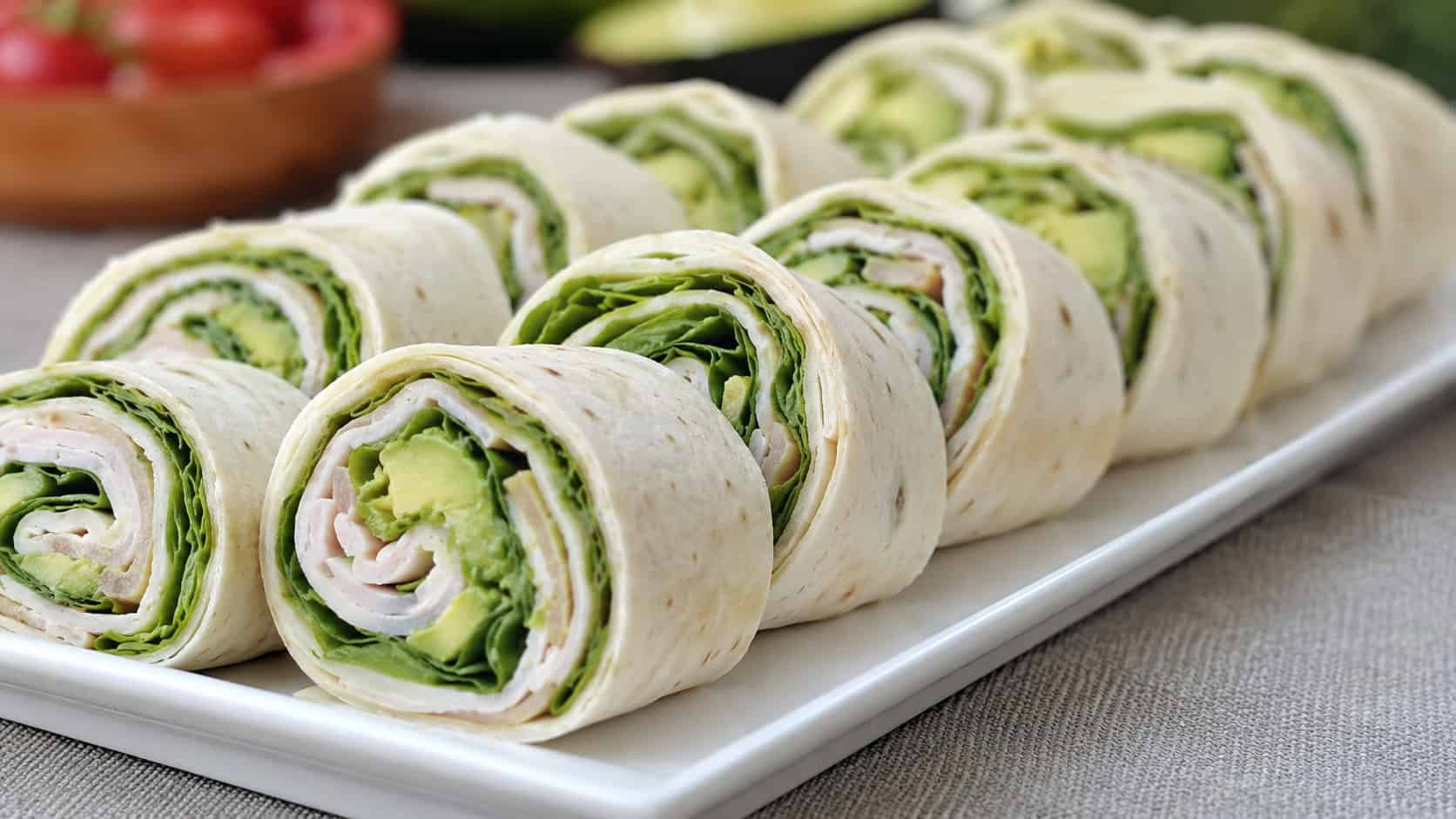 turkey and avocado pinwheel wraps sliced to show green avocado, turkey, and spinach spirals arranged on a platter, in a wide horizontal shot, natural light, shallow depth of field, landscape orientation