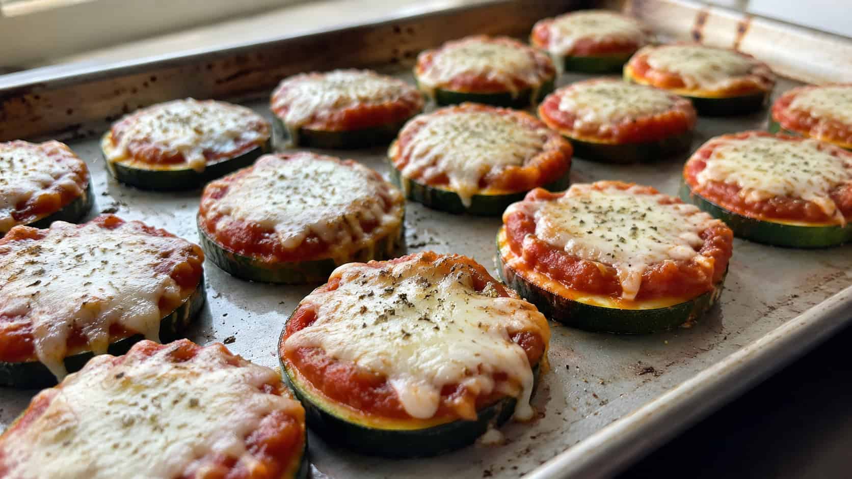 zucchini pizza bites topped with marinara and melted mozzarella and oregano on a baking sheet, in a wide horizontal shot, natural light, shallow depth of field, landscape orientation
