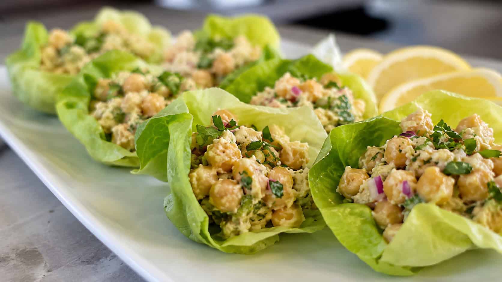 butter lettuce cups filled with lemony mashed chickpea salad arranged on a white platter, in a wide horizontal shot, natural light, shallow depth of field, landscape orientation