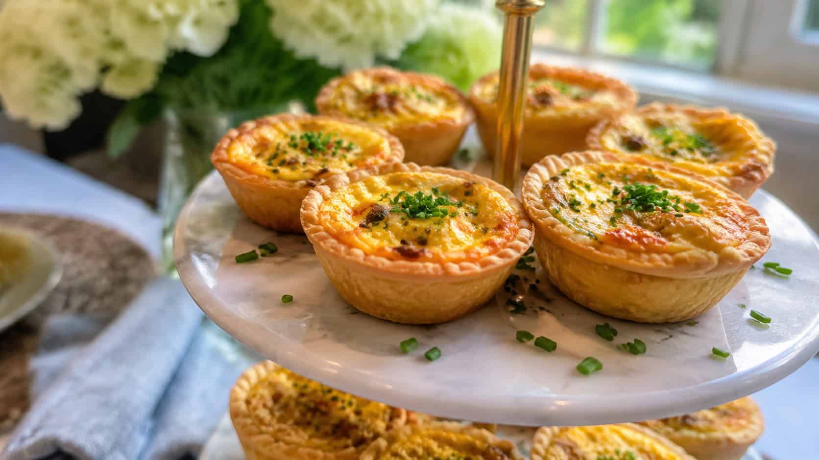 mini quiches with golden flaky crusts and fluffy egg filling in a wide horizontal shot, arranged on a tiered tray with chives, soft brunch natural light, shallow depth of field, landscape orientation