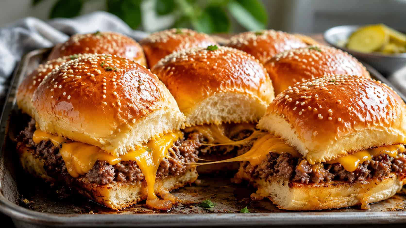 a tray of beef and cheddar sliders in a wide horizontal shot, glossy sesame-topped buns pulled slightly apart to show melted cheese, natural light, shallow depth of field, landscape orientation