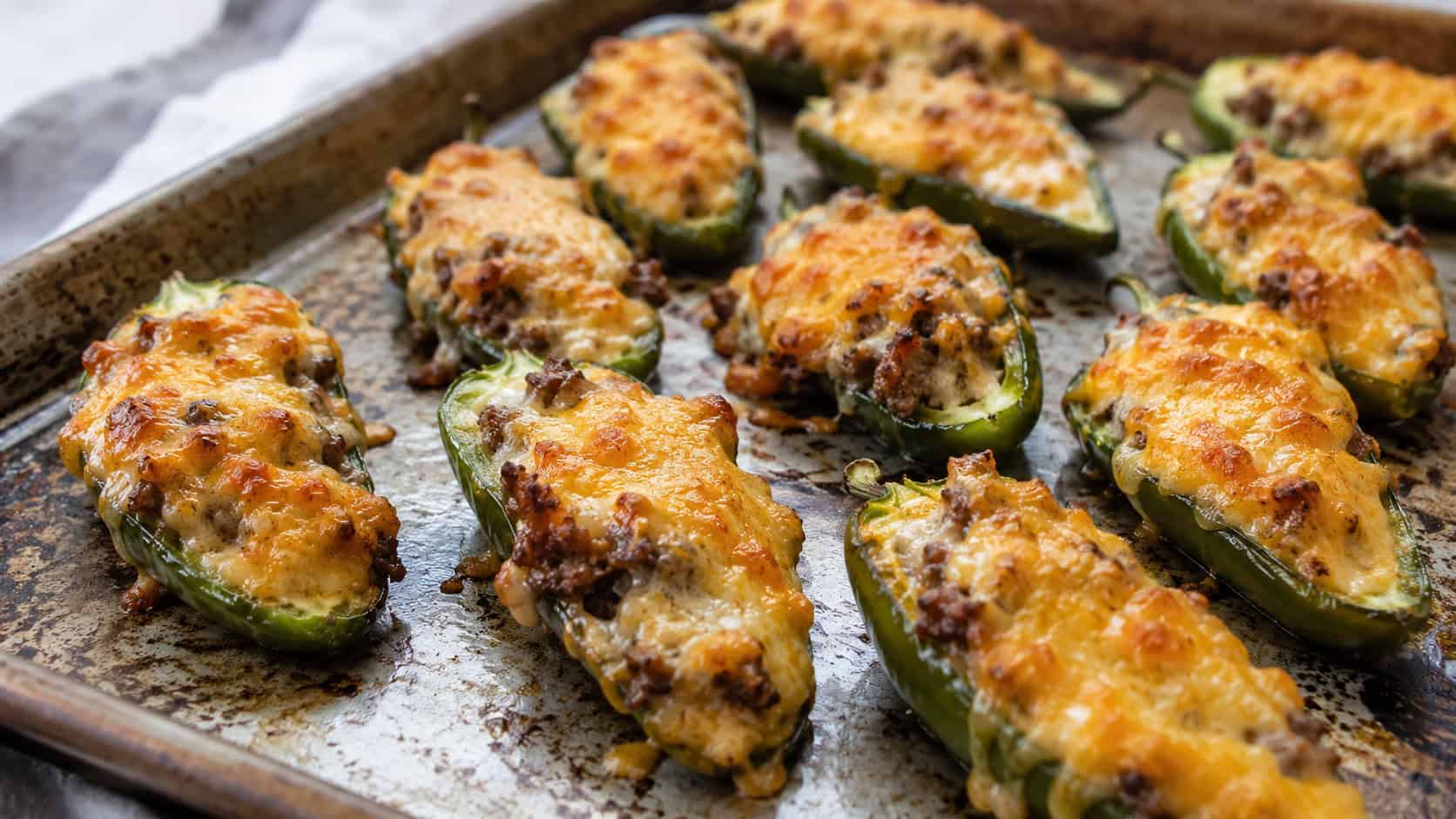 cheesy beef-stuffed jalapenos in a wide horizontal shot, golden bubbly tops on a rustic baking sheet, natural light, shallow depth of field, landscape orientation