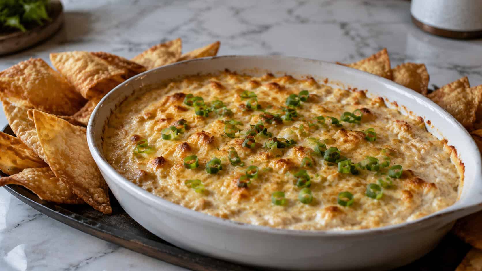 a baking dish of creamy crab rangoon dip in a wide horizontal shot, golden bubbling top and sliced green onions, surrounded by crispy wonton chips, marble countertop, warm natural light, shallow depth of field, landscape orientation