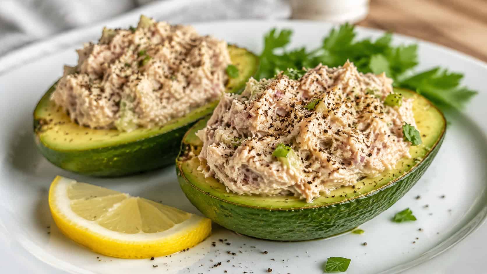 tuna stuffed avocados in a wide horizontal shot, green avocado halves filled with creamy tuna salad and a sprinkle of pepper, on a white plate with lemon, bright natural light, shallow depth of field, landscape orientation