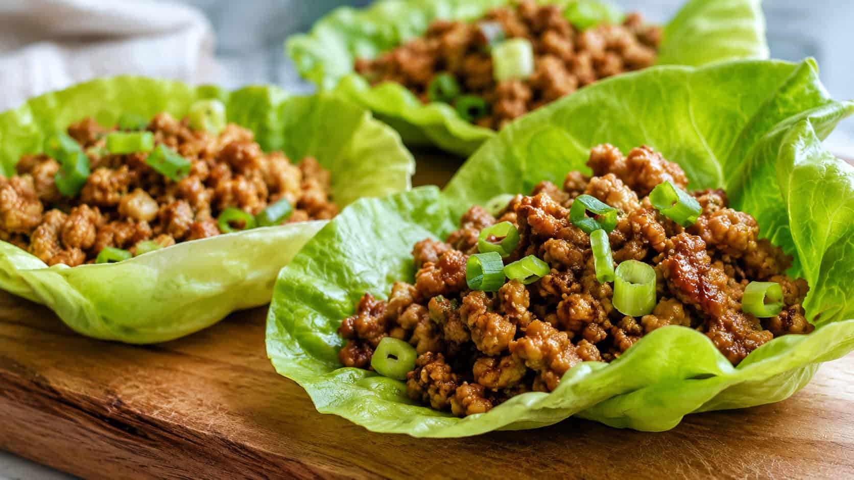 turkey lettuce wraps in a wide horizontal shot, crisp green lettuce cups filled with seasoned ground turkey and green onions, on a wooden board, bright natural light, shallow depth of field, landscape orientation