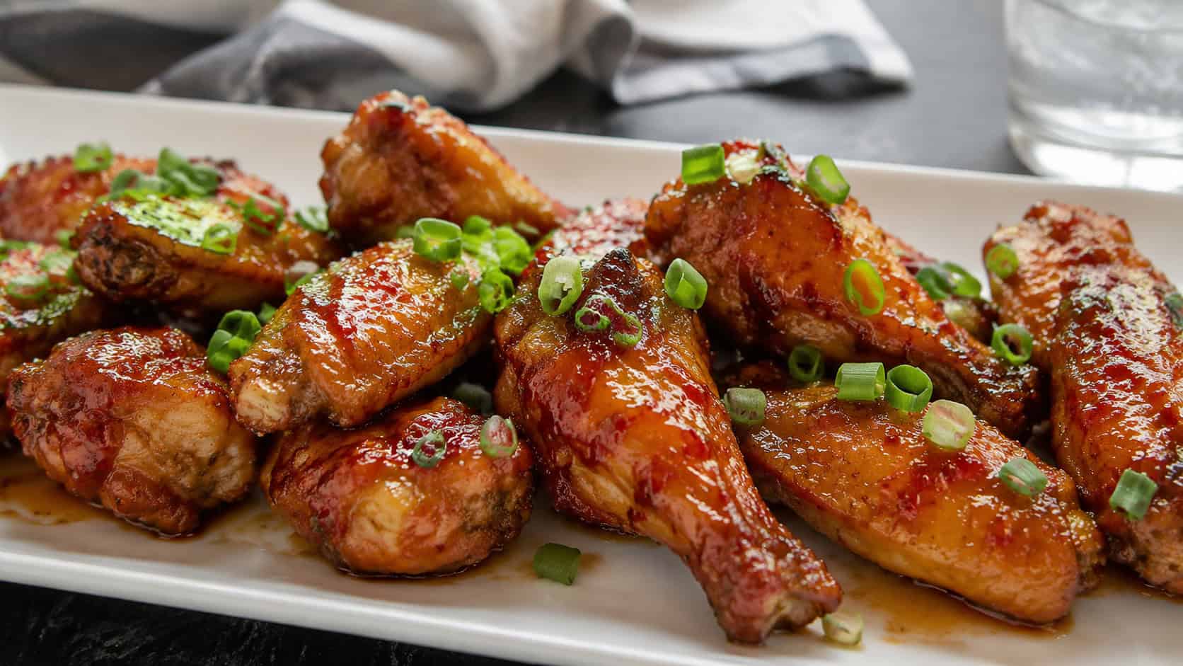 sweet chili chicken wings in a wide horizontal shot, glossy glazed wings topped with green onions on a platter, natural light, shallow depth of field, landscape orientation