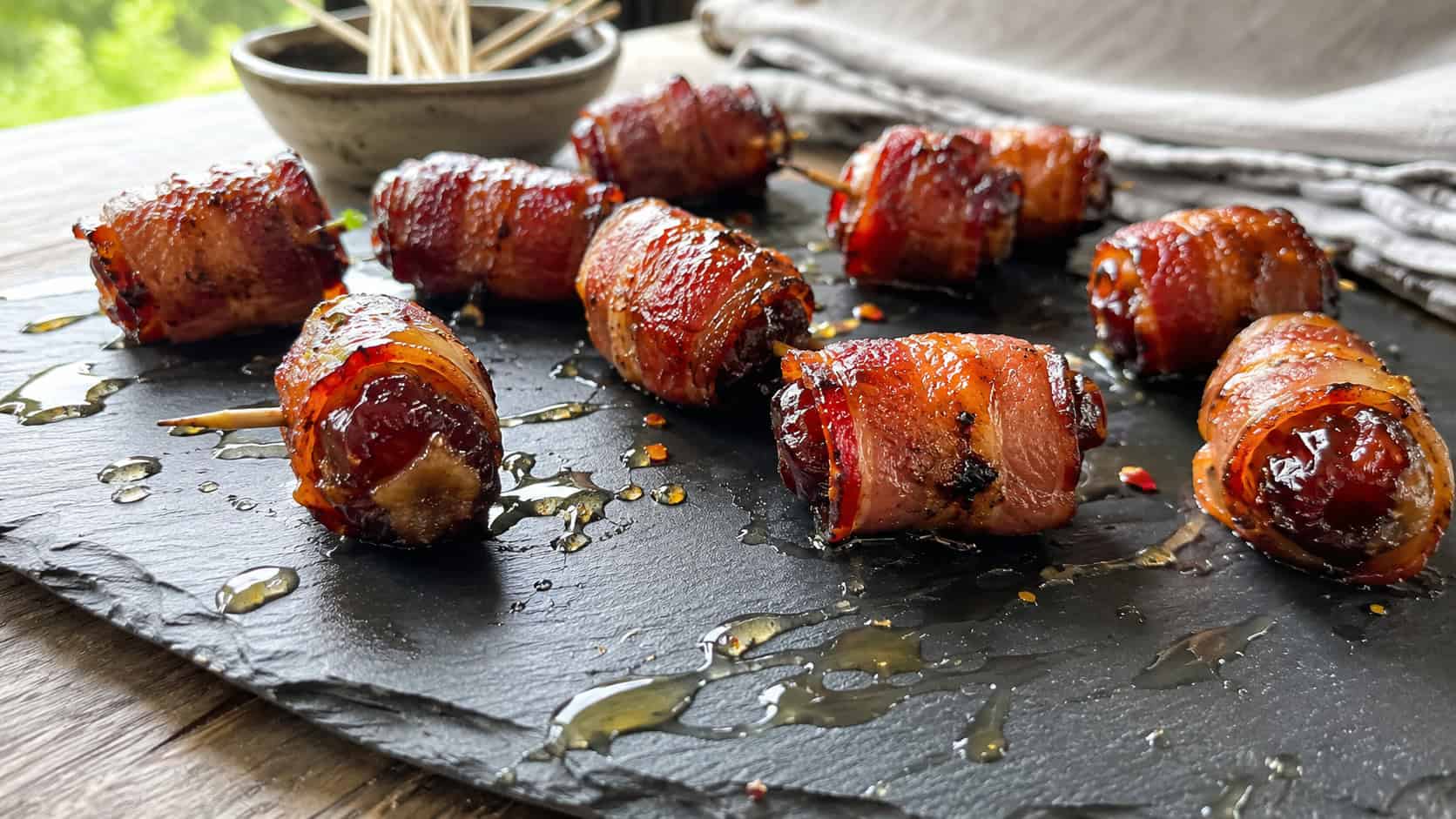 caramelized bacon-wrapped dates in a wide horizontal shot, glossy and crisp on a slate board drizzled with honey, natural light, shallow depth of field, landscape orientation