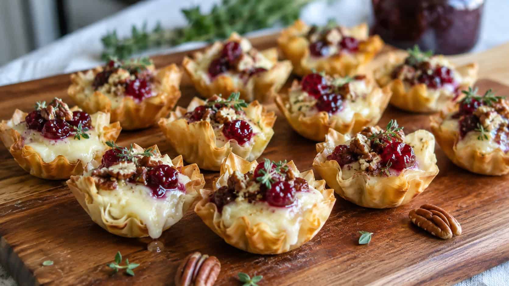 brie and cranberry phyllo cups in a wide horizontal shot, golden cups with melted cheese and ruby cranberry, pecans and thyme on a wooden board, natural light, shallow depth of field, landscape orientation