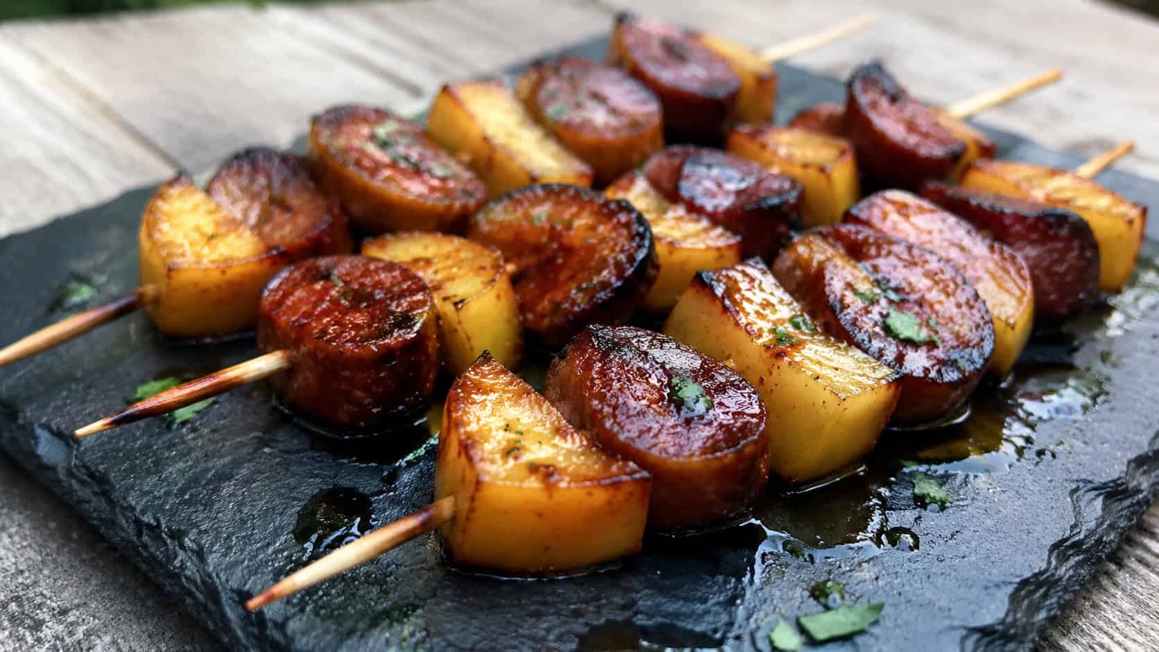 skewers with seared chorizo rounds and caramelized apple chunks in a wide horizontal shot, arranged on a slate board glistening with glaze, natural light, shallow depth of field, landscape orientation