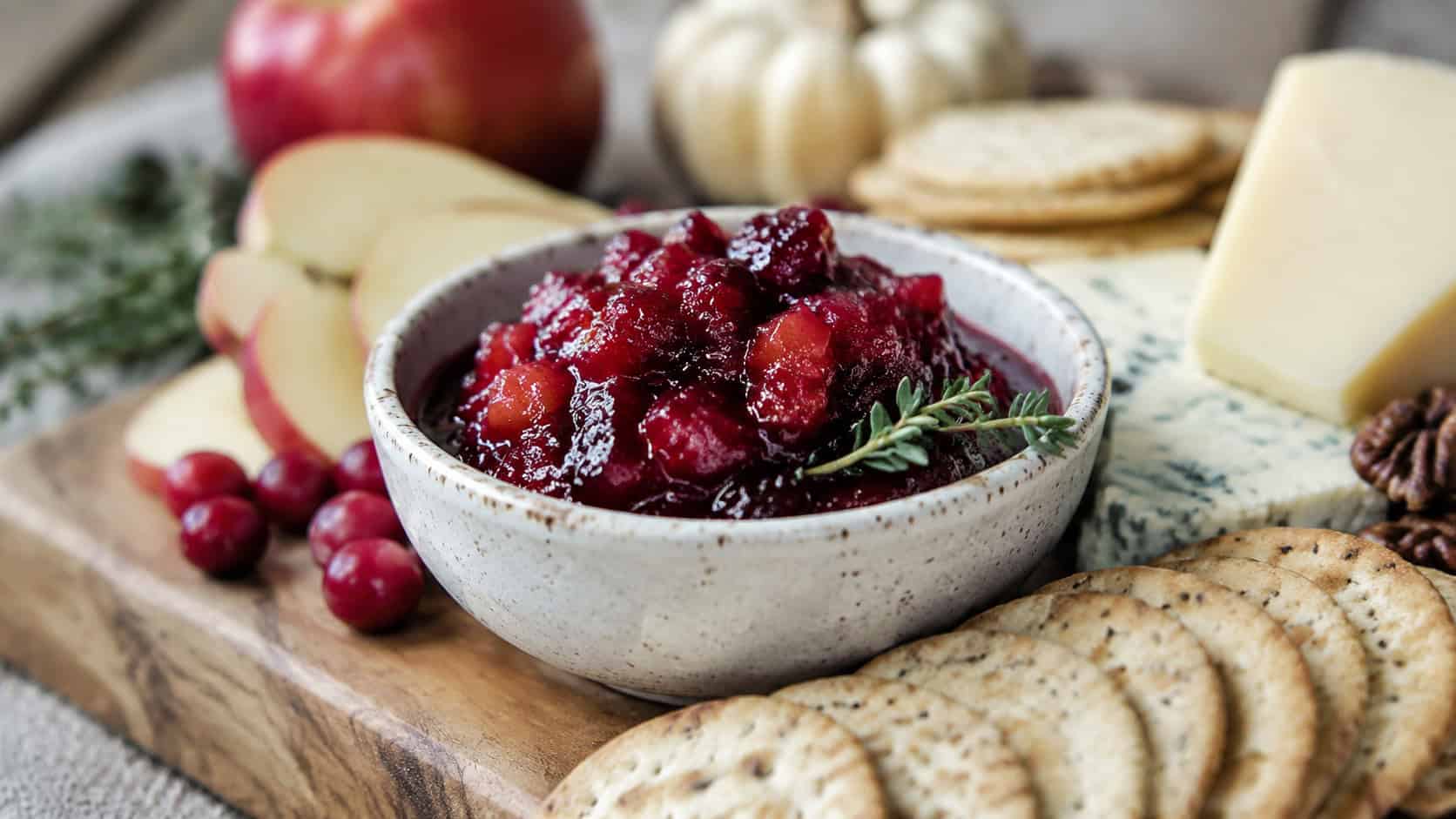 a bowl of jammy red apple cranberry chutney in a wide horizontal shot, set on a cheese board with crackers and cheese wedges, natural light, shallow depth of field, landscape orientation