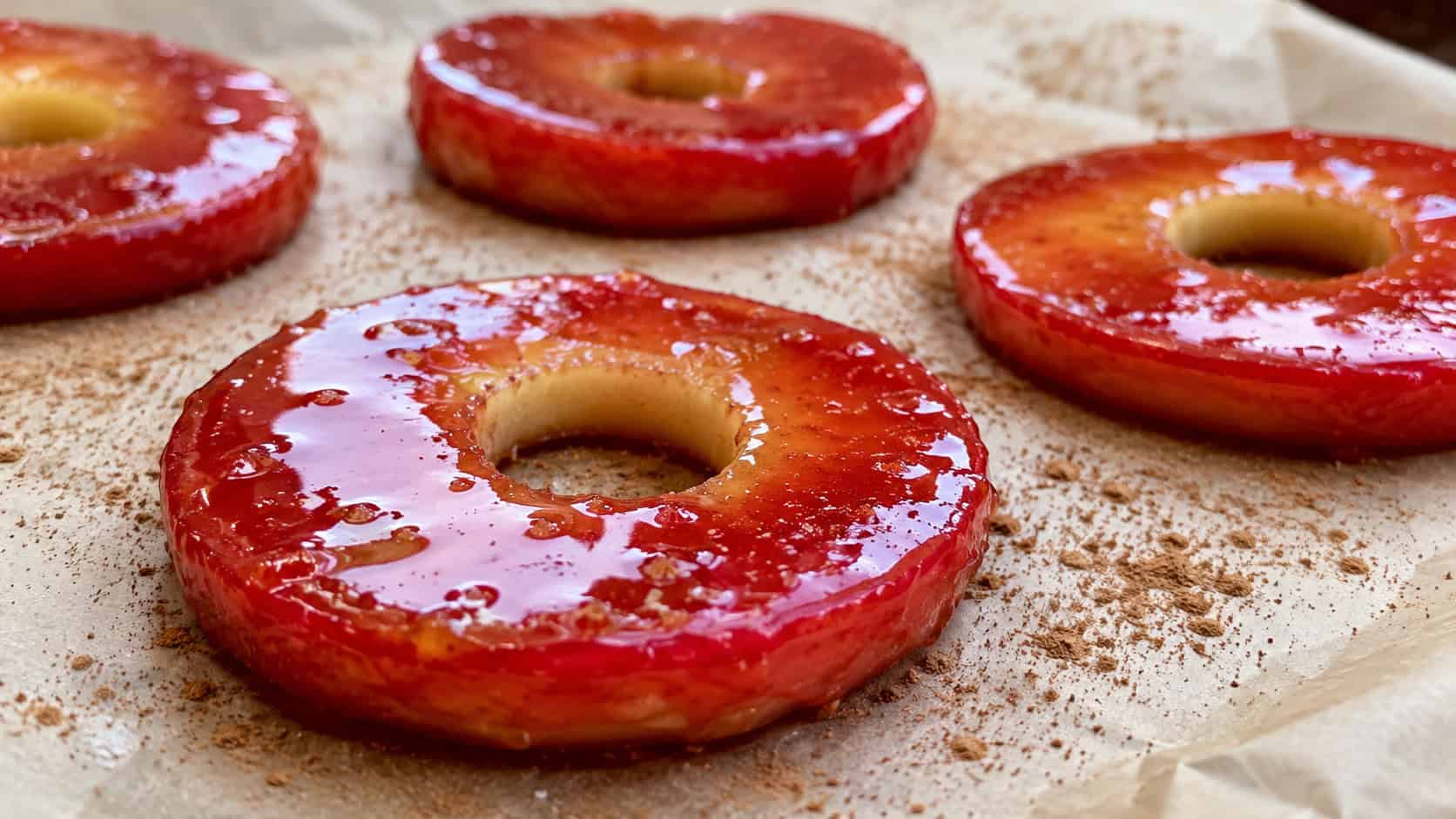 glossy red candied apple rings in a wide horizontal shot, arranged on parchment paper dusted with cinnamon, natural light, shallow depth of field, landscape orientation