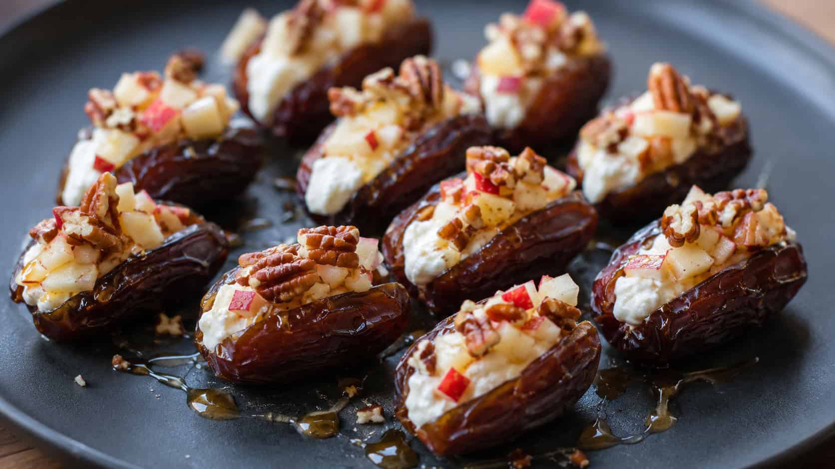 stuffed medjool dates filled with cream cheese and diced apple topped with pecans in a wide horizontal shot, arranged on a dark plate drizzled with honey, natural light, shallow depth of field, landscape orientation