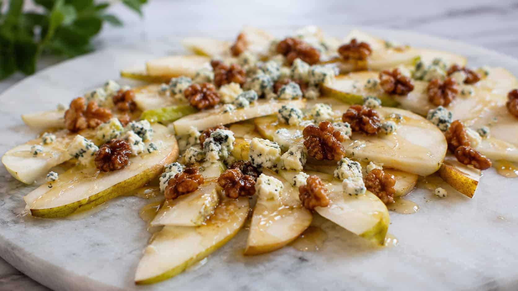 pear slices topped with crumbled blue cheese, candied walnuts, and honey in a wide horizontal shot, on a marble board, natural light, shallow depth of field, landscape orientation
