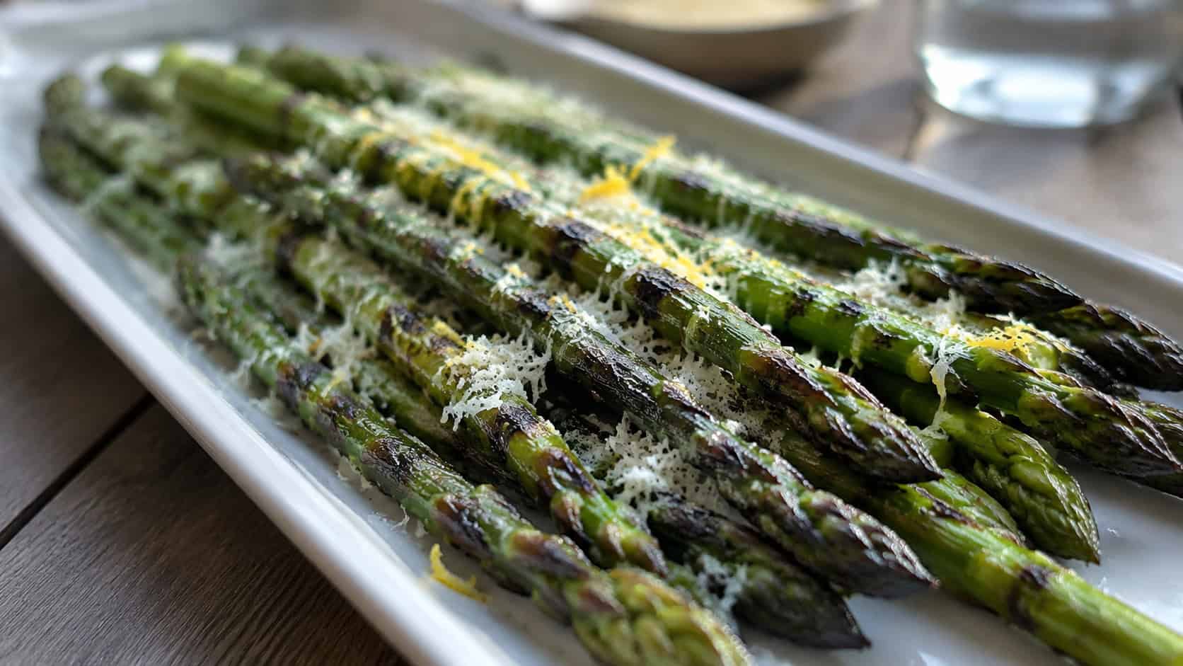 charred grilled asparagus spears topped with grated parmesan and lemon zest in a wide horizontal shot, on a long platter, natural light, shallow depth of field, landscape orientation