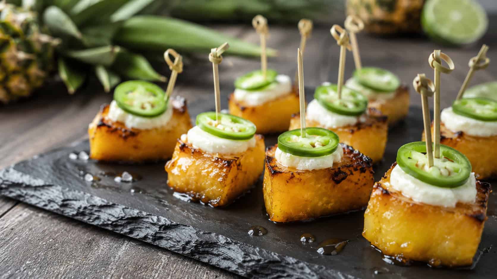 caramelized pineapple bites topped with cream cheese and jalapeño on a slate board in a wide horizontal composition, glossy honey glaze, cocktail picks standing up, bright natural light, shallow depth of field, landscape orientation