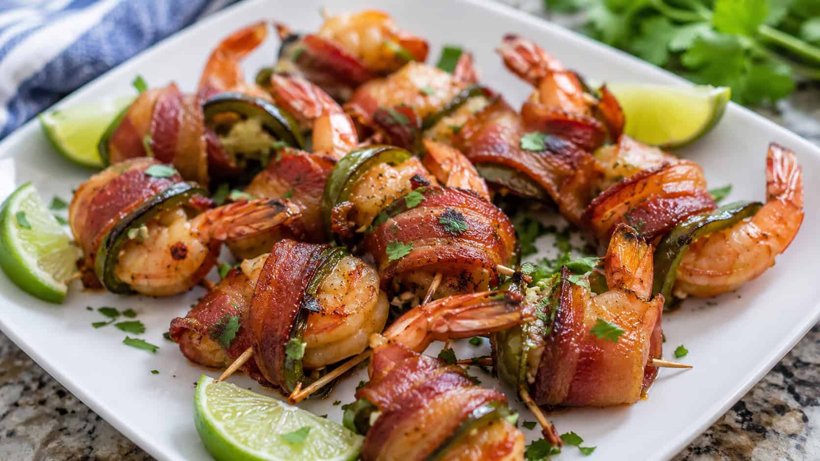 bacon-wrapped shrimp with jalapeño on a white platter in a wide horizontal composition, crispy bacon edges and pink shrimp, lime wedges scattered around, fresh herbs, natural light, shallow depth of field, landscape orientation
