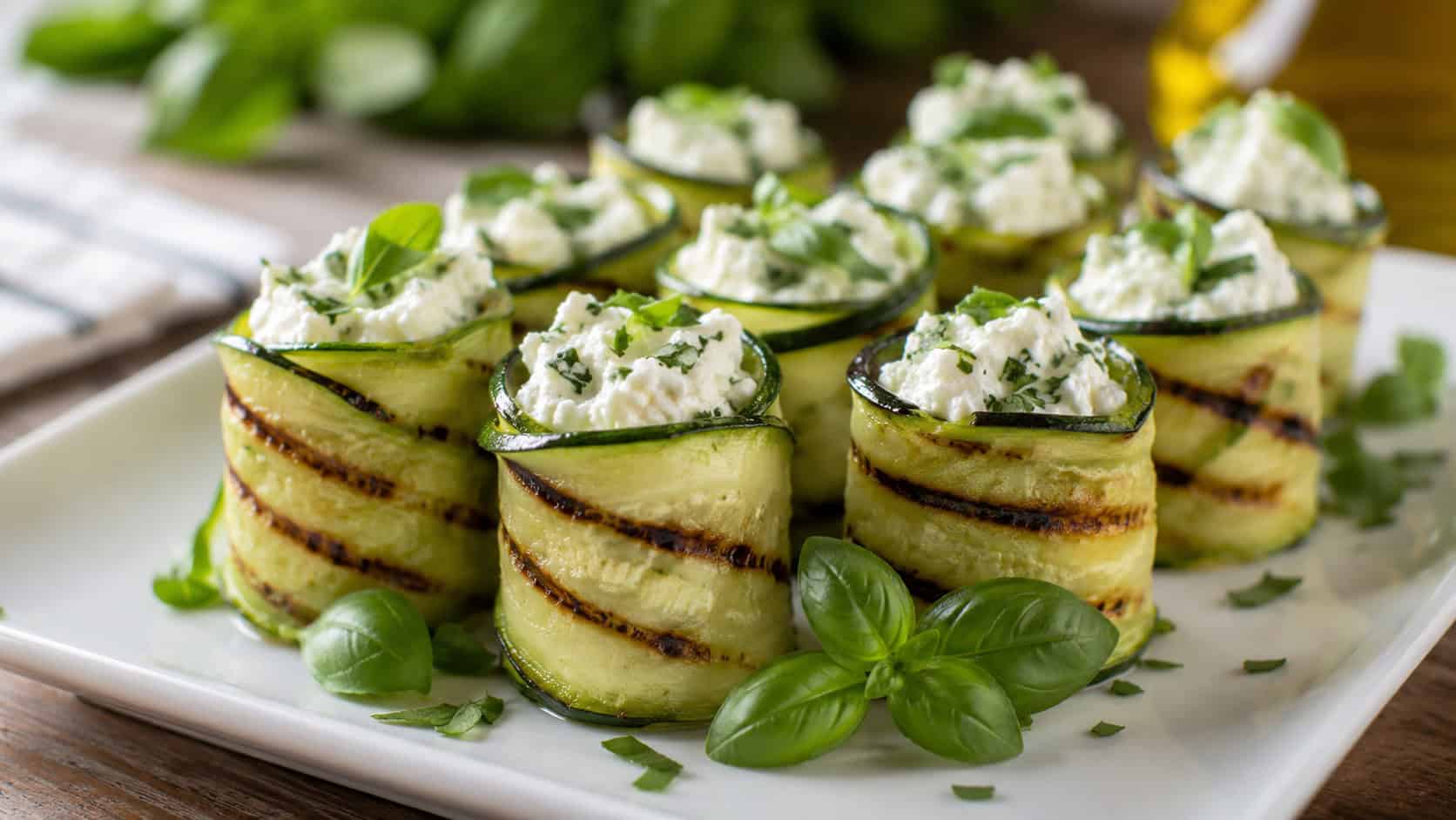 grilled zucchini ribbon roll-ups filled with herbed goat cheese standing upright on a white plate garnished with basil, in a wide horizontal shot, natural light, shallow depth of field, landscape orientation