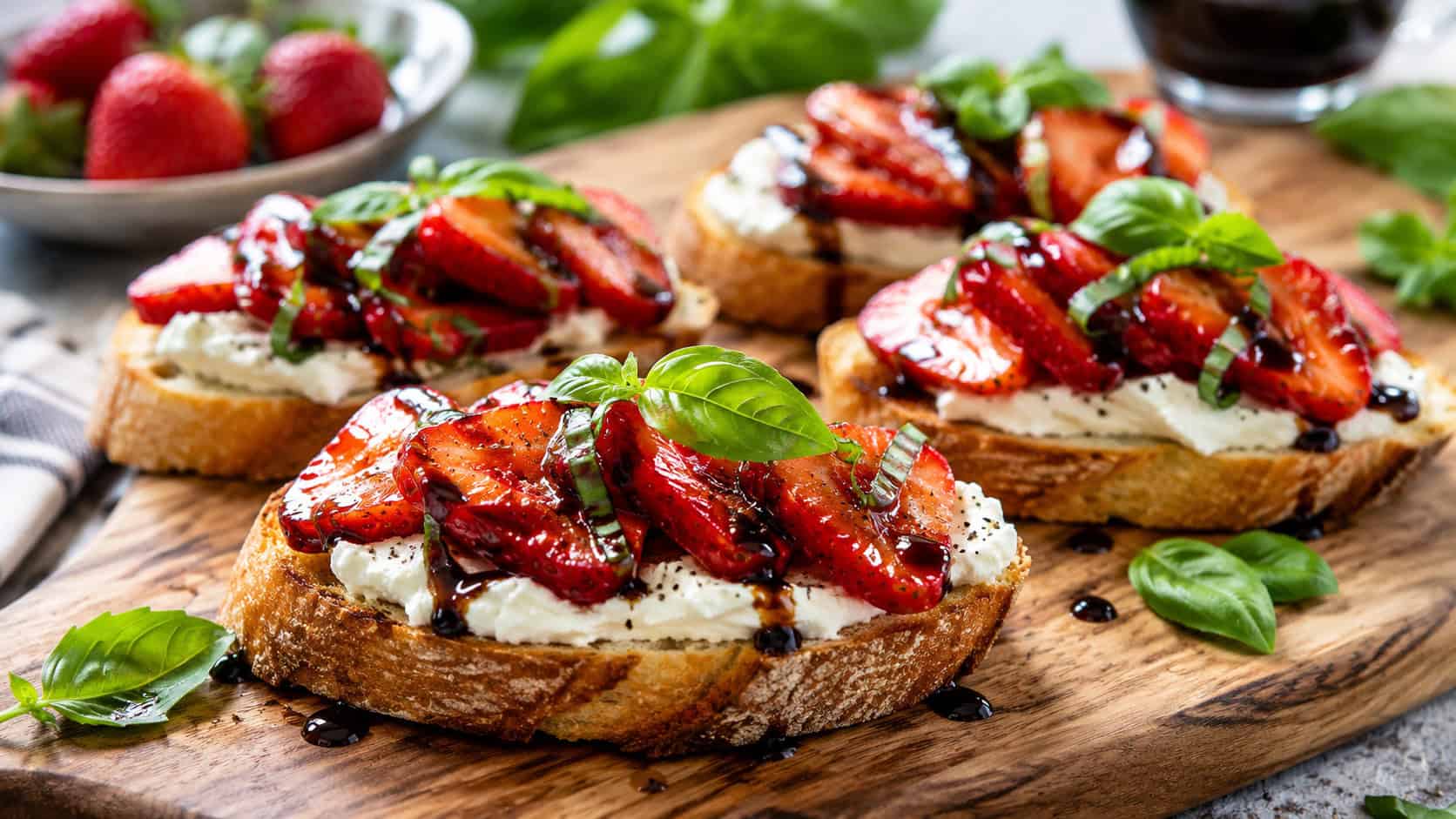 crostini topped with creamy goat cheese and glossy balsamic strawberries with basil leaves on a wooden board, in a wide horizontal shot, natural light, shallow depth of field, landscape orientation