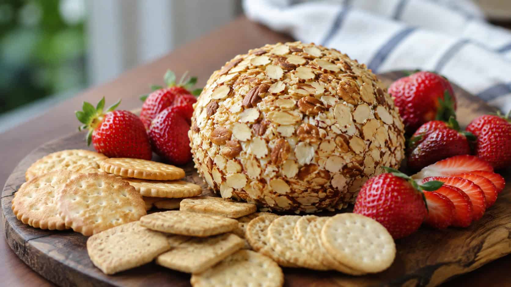 a strawberry cheese ball coated in toasted almonds on a wide horizontal wooden board surrounded by crackers and fresh strawberries, soft natural light, shallow depth of field, landscape orientation