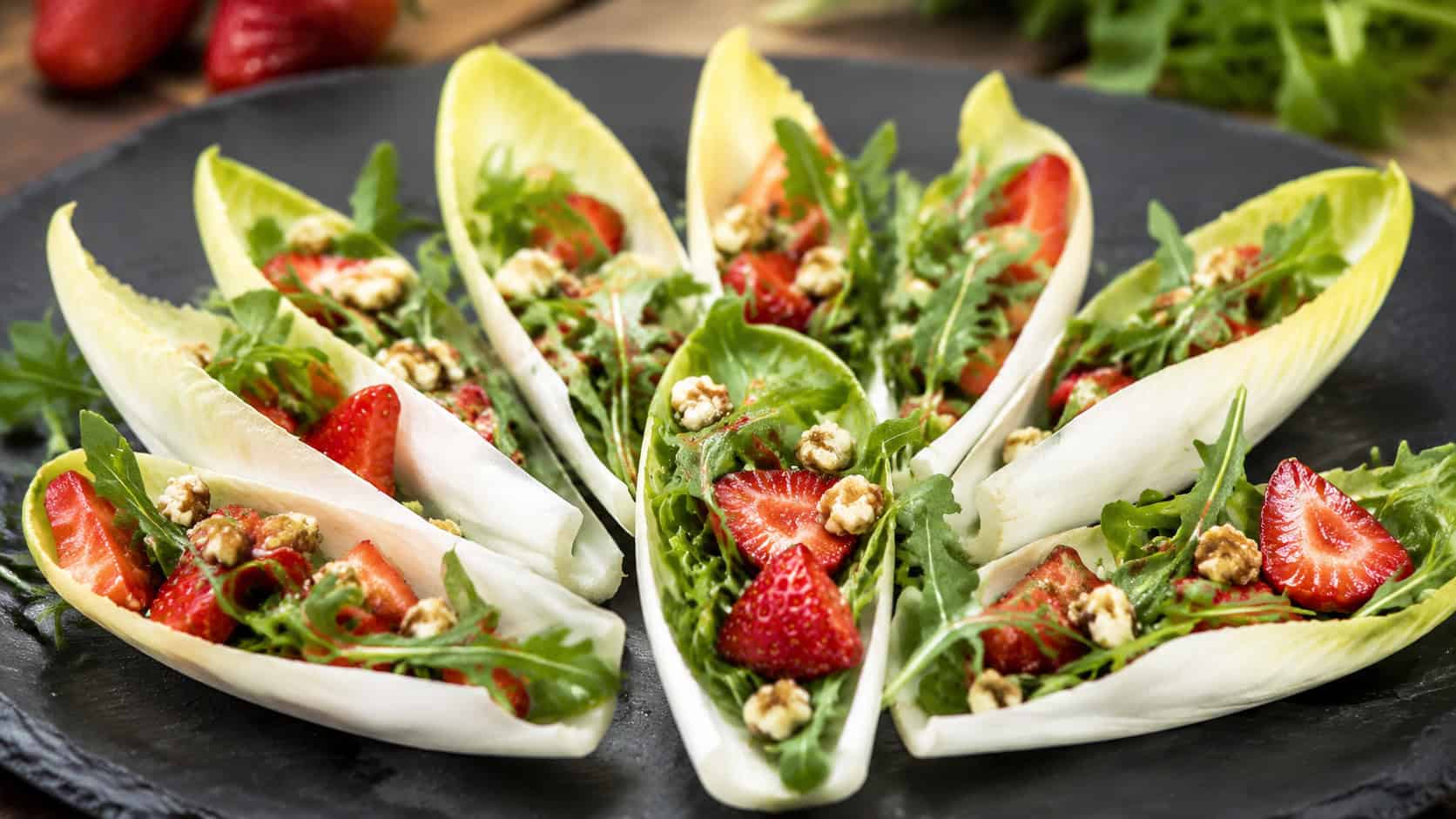 endive leaves filled with strawberry arugula salad and chopped walnuts, arranged in a wide horizontal fan on a slate board, fresh and vibrant, bright natural light, shallow depth of field, landscape orientation